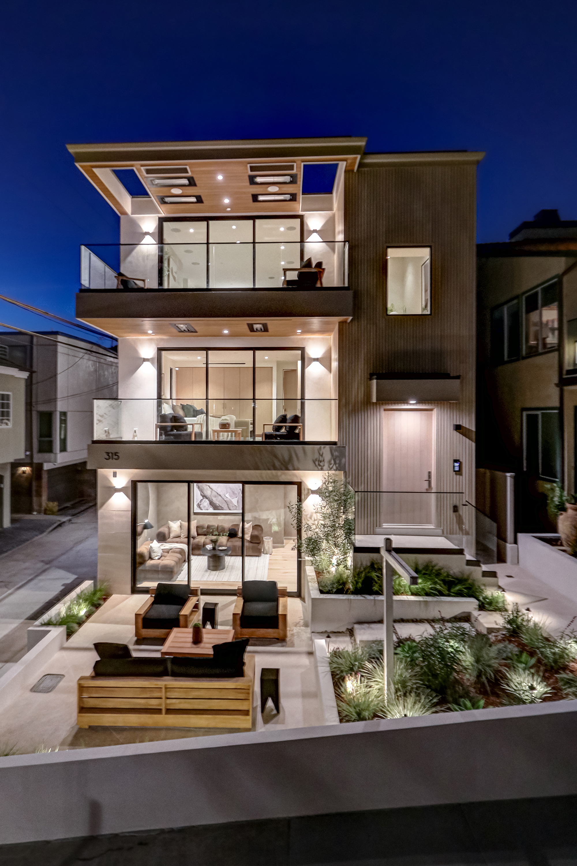 Twilight exterior of 315 25th Street, a custom three-story modern coastal residence in Manhattan Beach with illuminated balconies and corner walk-street position