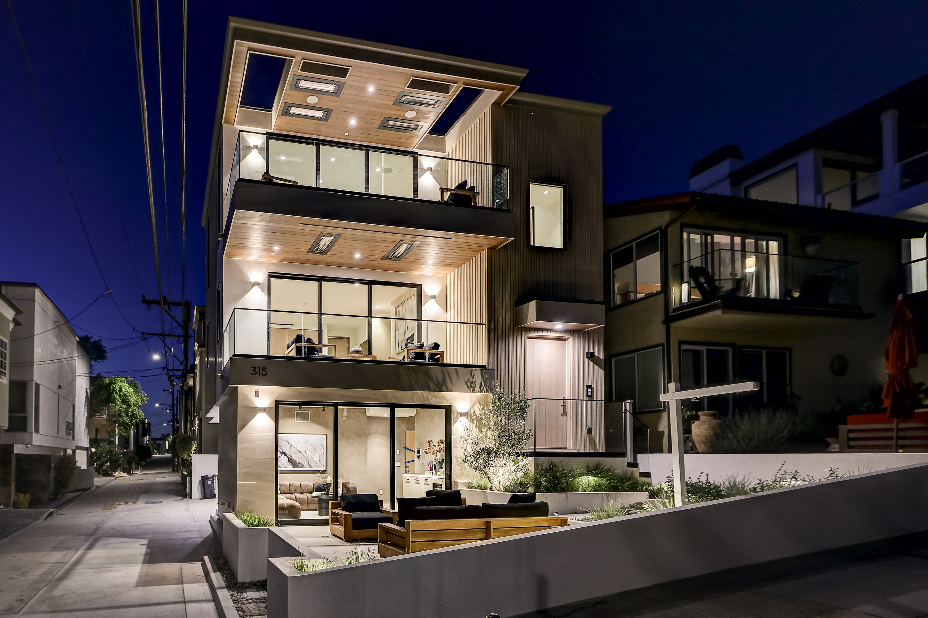 Twilight exterior with illuminated facade, glass balconies, and patio seating area